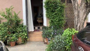 Une cour avec une porte en bois, des plantes en pot et une voiture garée à l’extérieur.