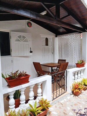 A covered outdoor seating area with a table and chairs, surrounded by potted plants and a white railing. - Simple Living: Live Like A Local (Mount Helicon)