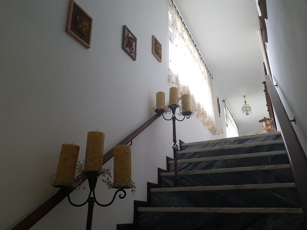 Una escalera con barandilla, un candelabro y tres cuadros enmarcados en la pared.