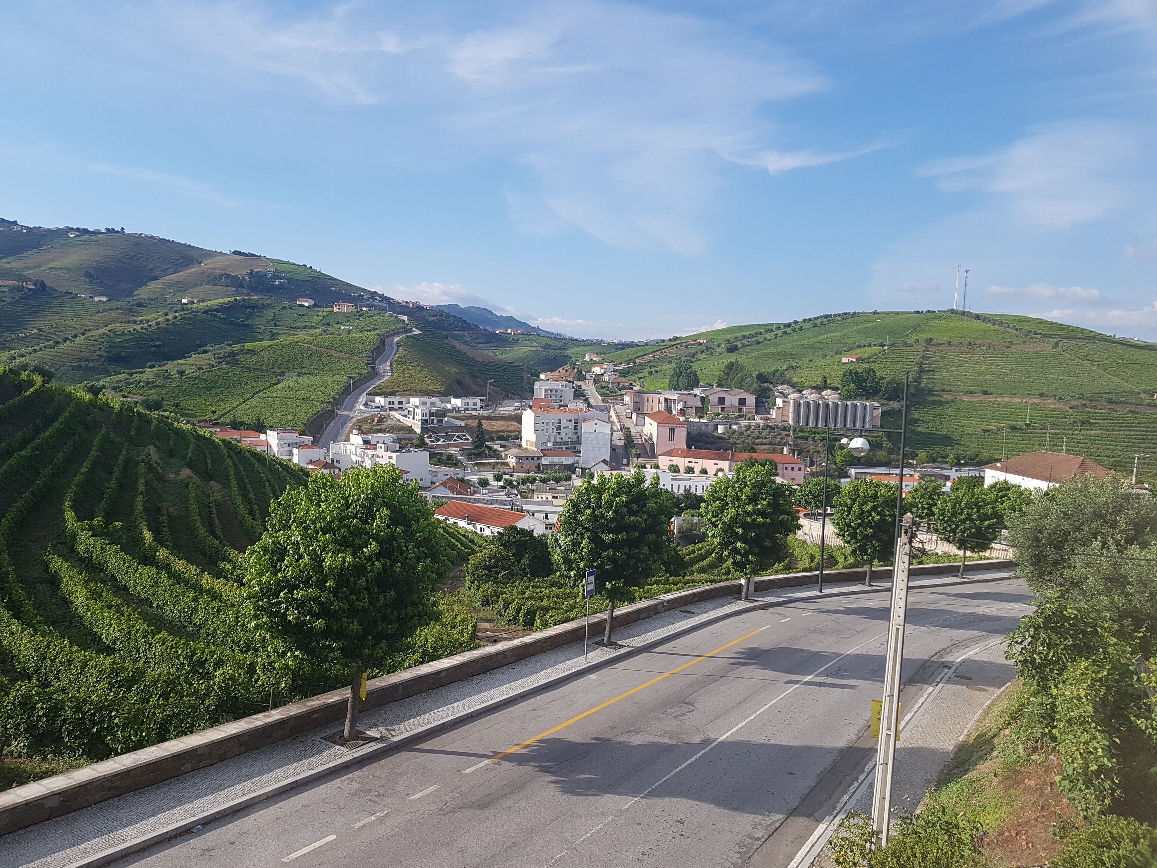 Una carretera serpentea por un pueblo con edificios y colinas verdes al fondo.