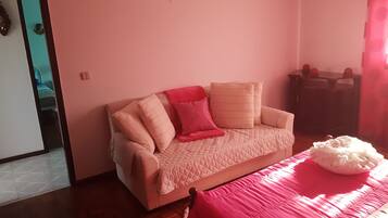 Ett rum med en beige soffa, en röd pläd och ett rosa sängöverkast.