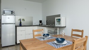 Une cuisine moderne avec des meubles blancs, un four à micro-ondes et une machine à café. On y trouve une table à manger en bois avec des chaises, un vase avec une plante et un set de table bleu et blanc.