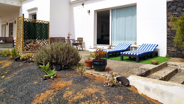 Une maison moderne dotée d’un patio comprenant deux fauteuils de jardin à rayures bleues et une petite table.