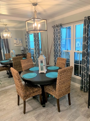 A dining area with wicker chairs, a round table, and a chandelier.