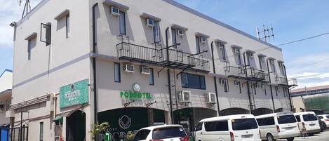 A multi-story building with a sign for 'PODDOTEL' and several parked white vans.
