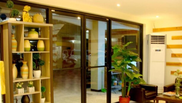 A modern living room with a sliding glass door leading to a balcony, a wooden bookshelf filled with decorative items, and a potted plant on a wooden table. - Airport Poddotel (Pasay)