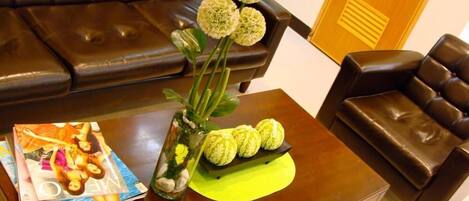 A living room with a brown leather sofa, a coffee table with a magazine, a vase with flowers, and a yellow placemat.