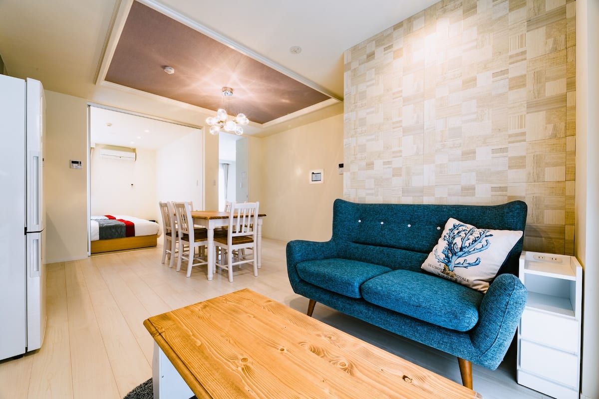 A modern living room with a blue sofa, wooden coffee table, and a dining area with chairs and a table.