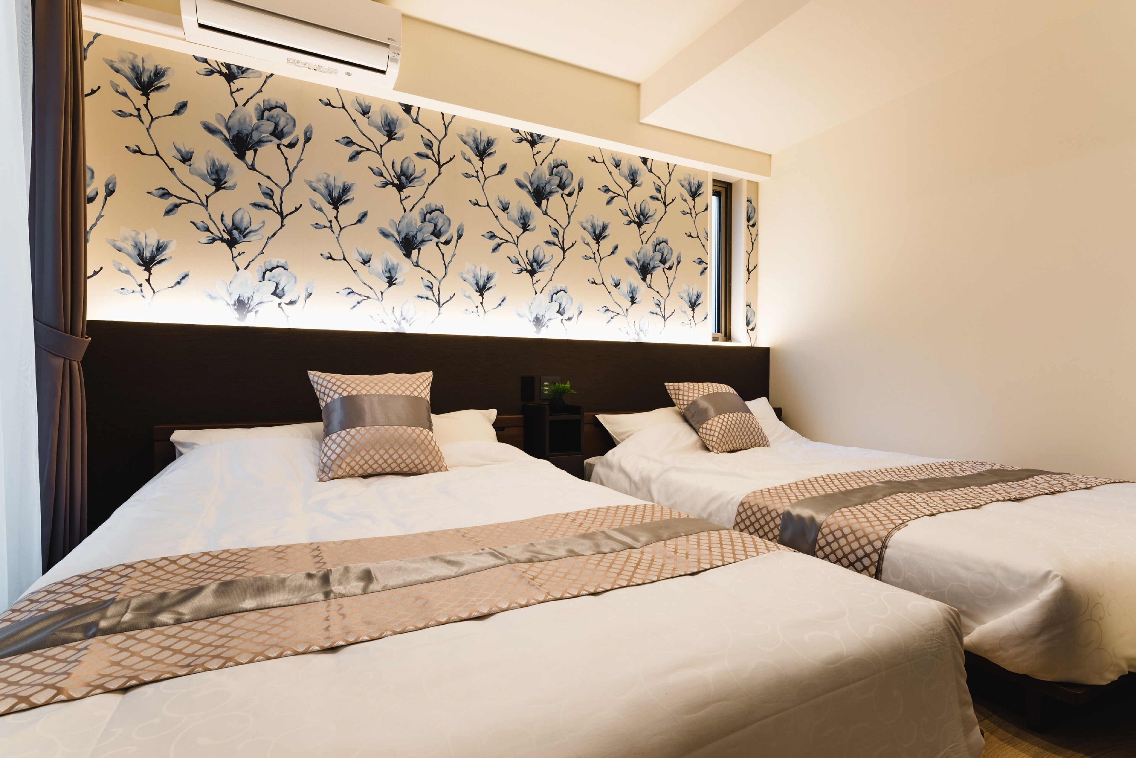 A hotel room with two beds, a floral headboard, and a nightstand with a lamp.