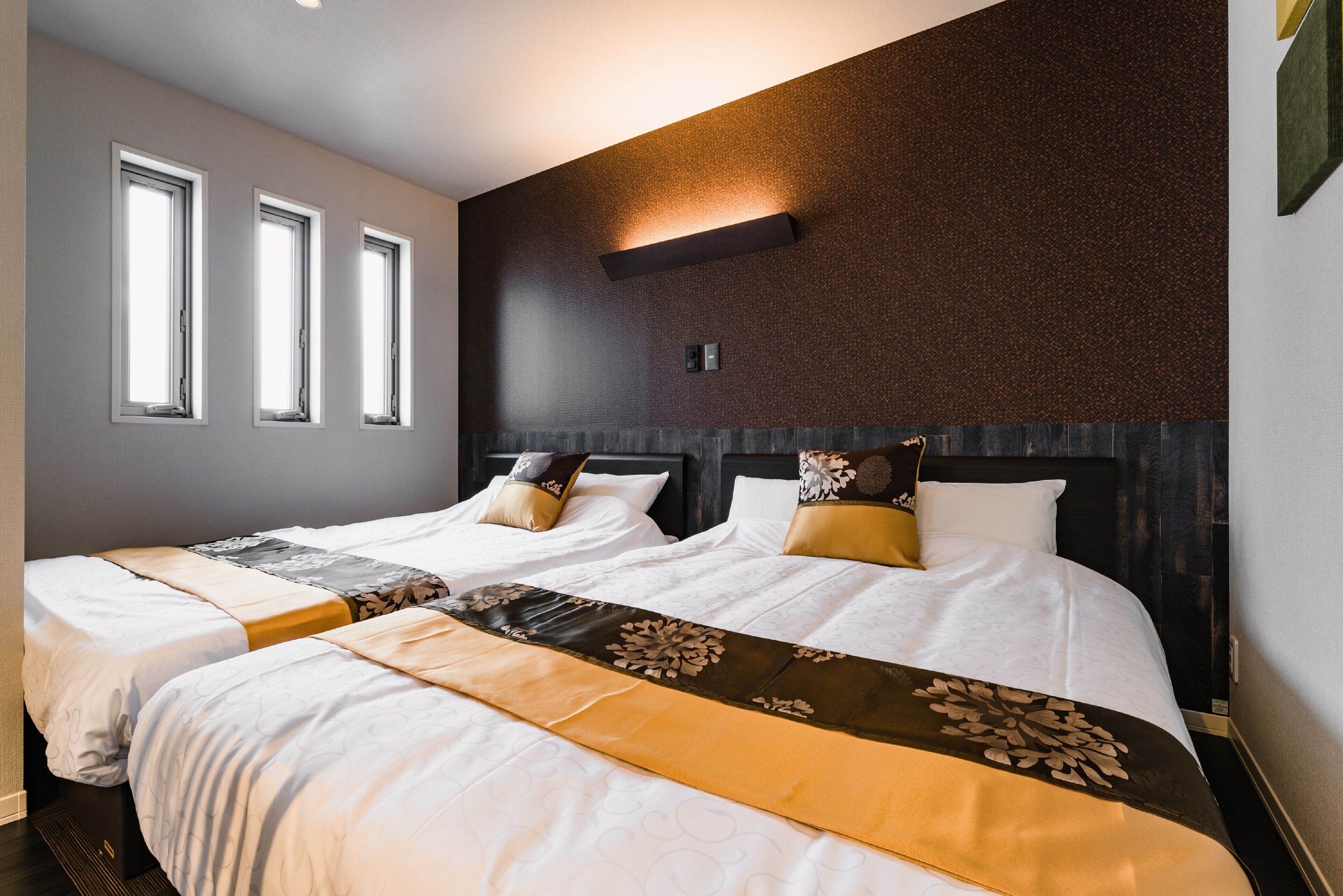 Habitación de hotel con dos camas, una pared oscura con textura y una ventana con persianas.