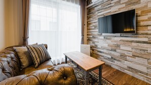 A living room with a leather sofa, a wooden coffee table, and a flat-screen TV mounted on a wooden wall. - HOTEL -sui- HARUYOSHI (Fukuoka)