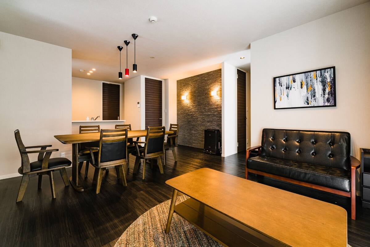 A modern living room with a wooden dining table, chairs, a sofa, and a fireplace.