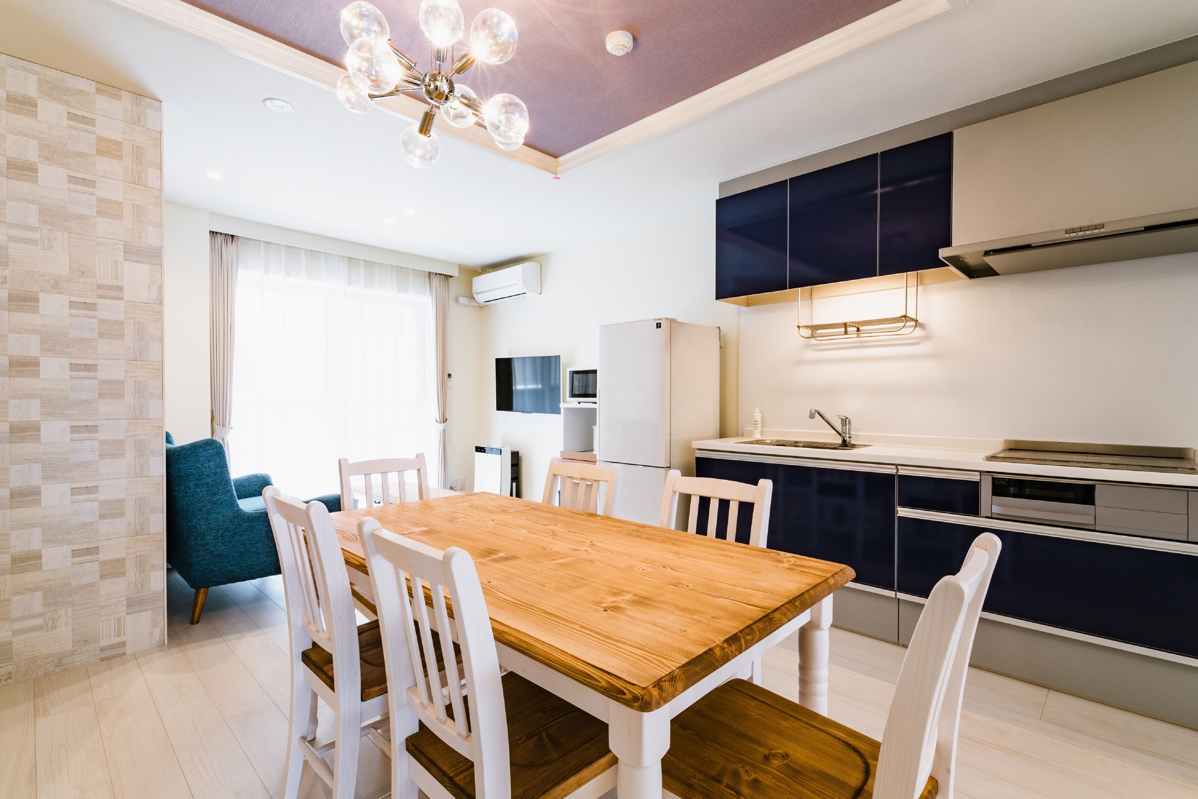 A modern kitchen with white cabinets, a wooden dining table, and a blue chair.