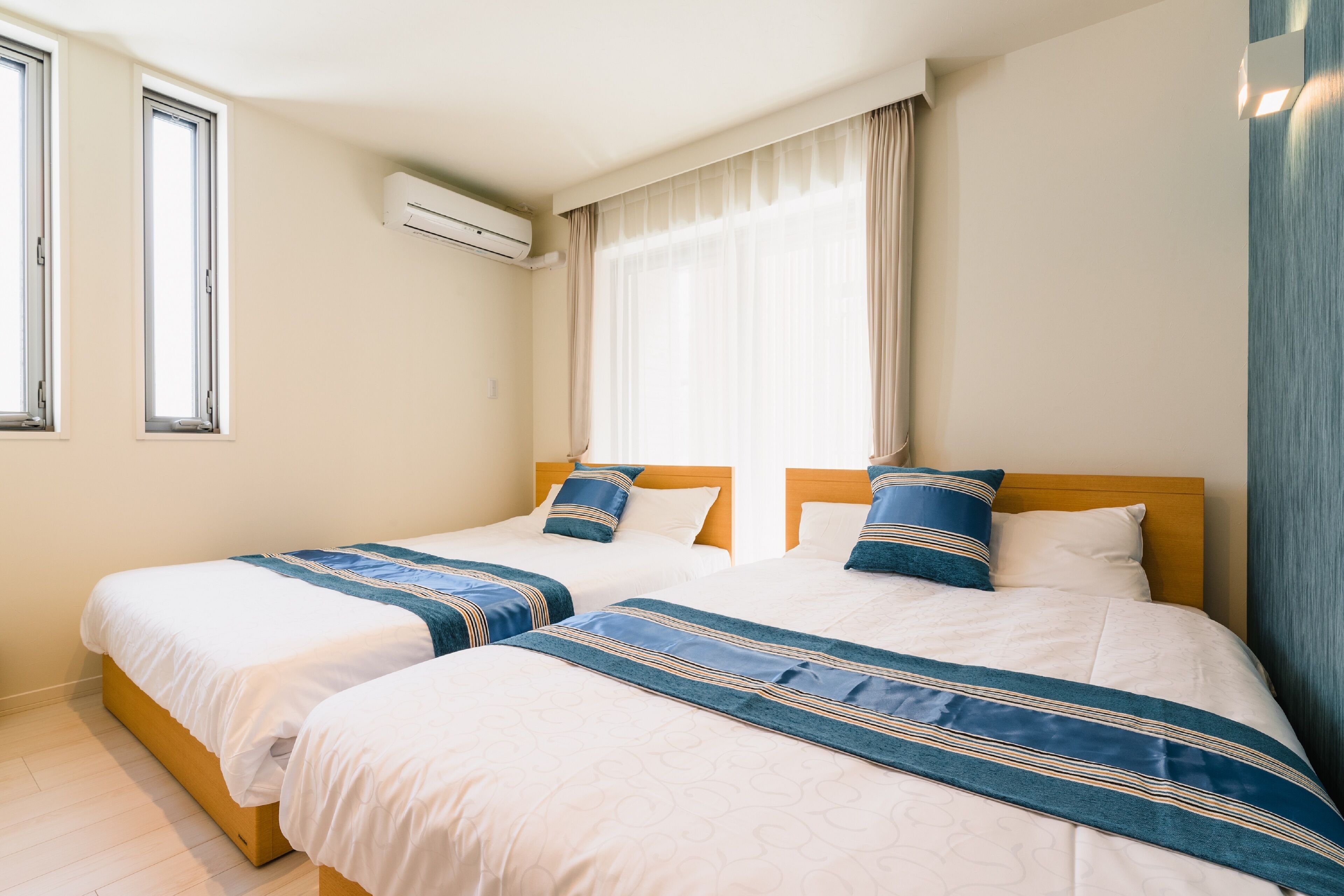 Une chambre d’hôtel avec deux lits, des murs de couleur beige, une fenêtre avec des rideaux et un appareil de climatisation.