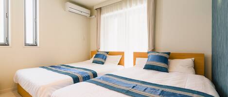 Une chambre d’hôtel avec deux lits, des murs de couleur beige, une fenêtre avec des rideaux et un appareil de climatisation.