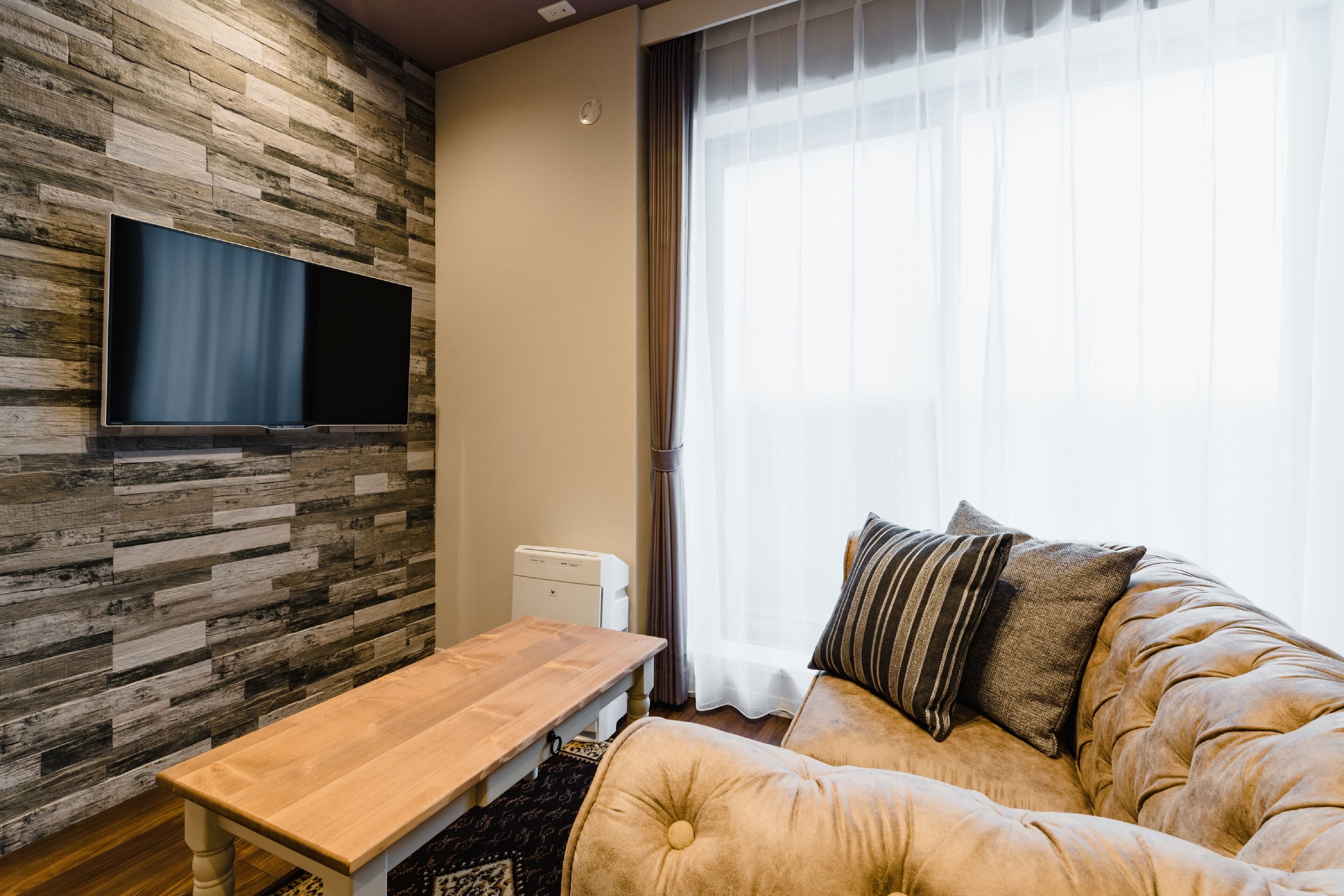 A living room with a wooden wall, a flat-screen TV, a sofa, and a window with curtains.