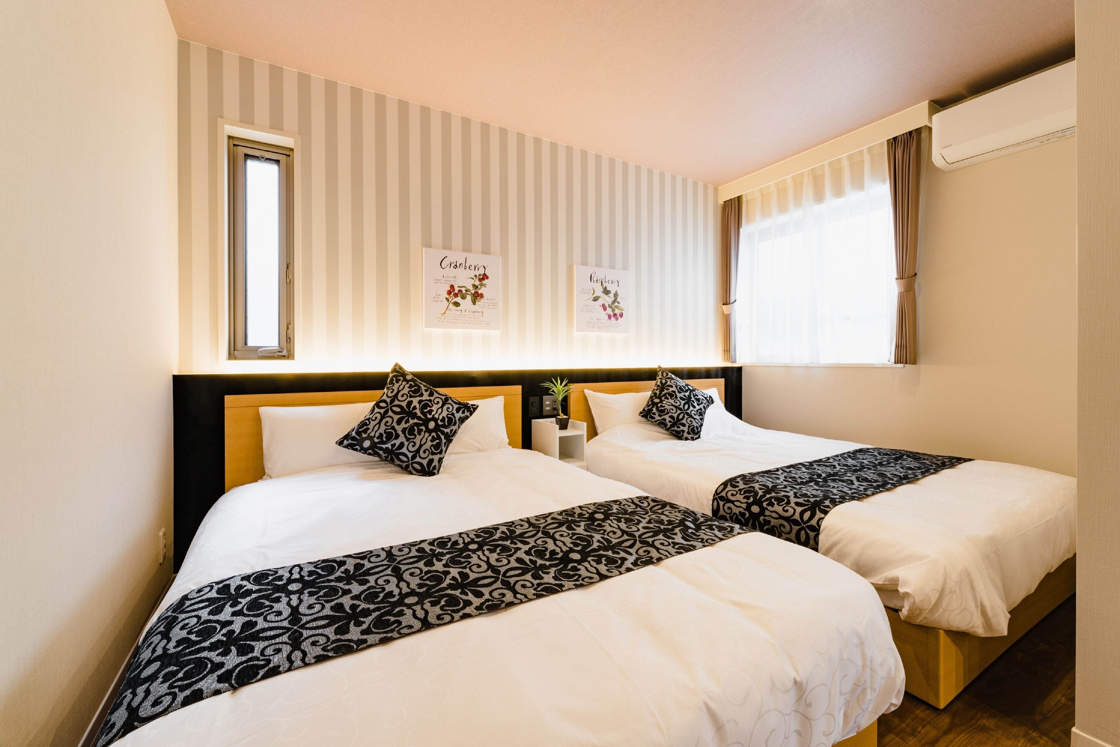 A hotel room with two beds, striped wallpaper, and framed botanical prints on the wall.
