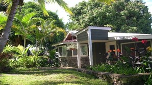 Ein Haus mit einer Steinfassade, einer überdachten Veranda und einem Garten mit tropischen Pflanzen.