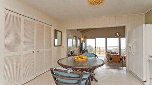 A dining area with a round table, chairs, and a fruit bowl. There is a sliding door on the left and a refrigerator on the right.