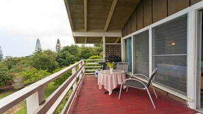 A covered balcony with a red floor, a table with a checkered tablecloth, and a grill.