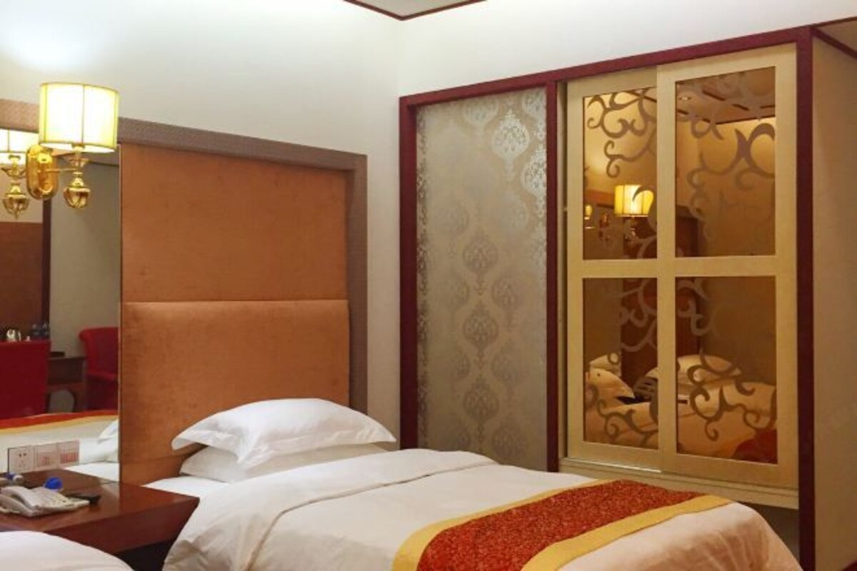 A hotel room with a large bed, a wooden headboard, a bedside table with a lamp, and a decorative screen with a patterned design.