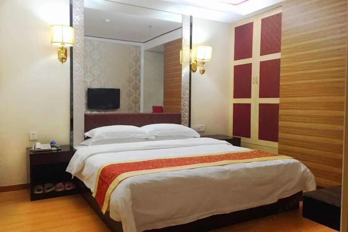 A hotel room with a large bed, two bedside tables, a TV, and a mirror.