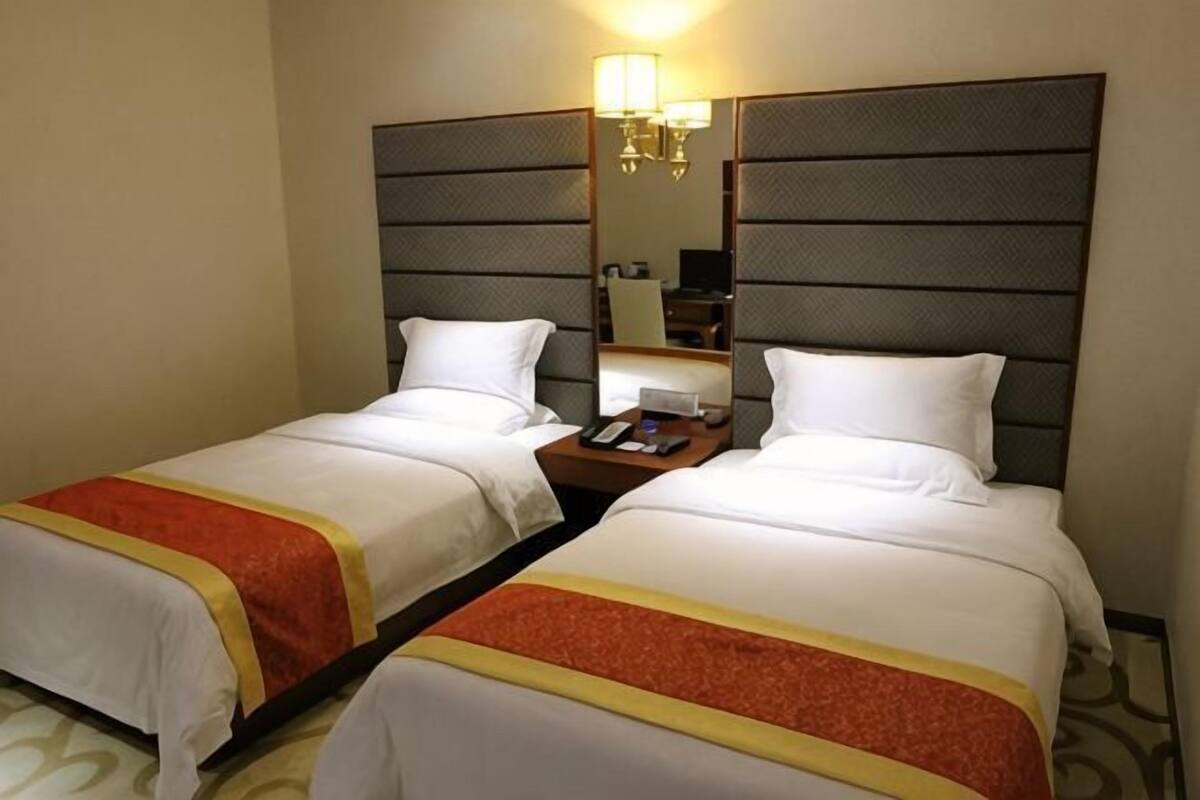 A hotel room with two beds, a nightstand, a lamp, and a mirror.