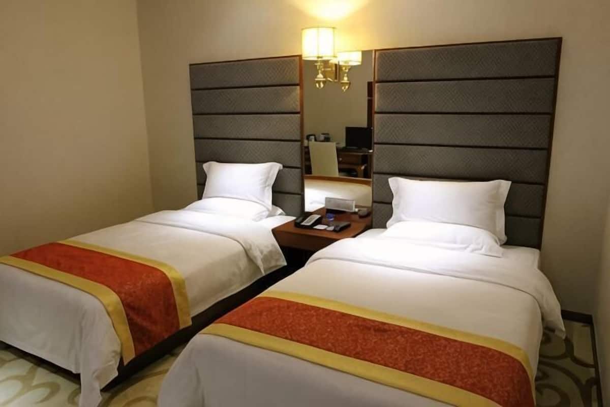 Una habitación de hotel con dos camas, una mesita de noche, una lámpara y un espejo.