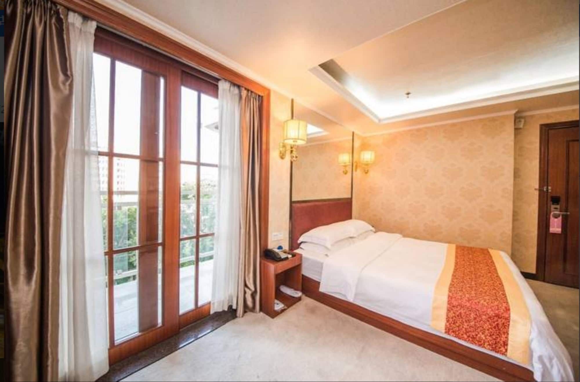 A hotel room with a large window, a bed, a bedside table, and a door.