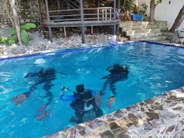 Una piscina con agua azul cristalina, rodeada de baldosas de piedra y una terraza de madera.