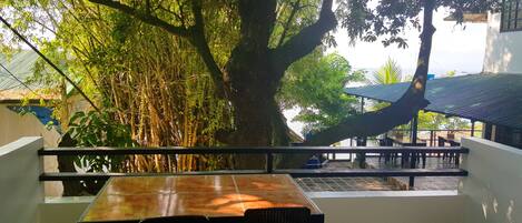 A terrace with a table and chairs, surrounded by lush greenery and a large tree.