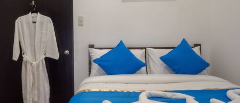 Hotelkamer met een bed, twee blauwe kussens, een witte badjas hangend aan een deur en een schilderij aan de muur.