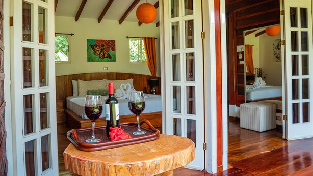 A room with a bed, a dining table with wine glasses and a bottle, and a wooden floor.