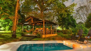 A pool area with a wooden gazebo, lounge chairs, and lush greenery.