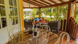 An outdoor patio with wicker furniture, a glass table, and a bottle of wine.