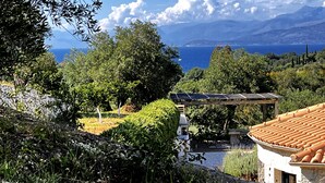 Un jardín con un pérgola, vistas al mar y un edificio con techo de tejas.