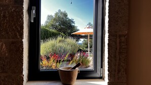 Una ventana con vista a un jardín, una puerta de madera y un muro de piedra.