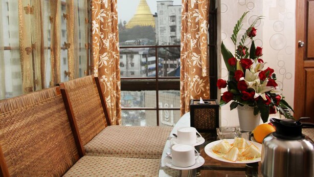 A room with a sofa, a table with a tea set, a vase of flowers, and a view of a golden pagoda through sheer curtains. - Crystal Palace Hotel (Yangon)