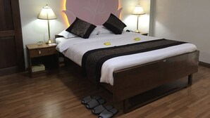 A neatly made bed with a large headboard, two bedside lamps, and a wooden nightstand with a clock. - Crystal Palace Hotel (Yangon)