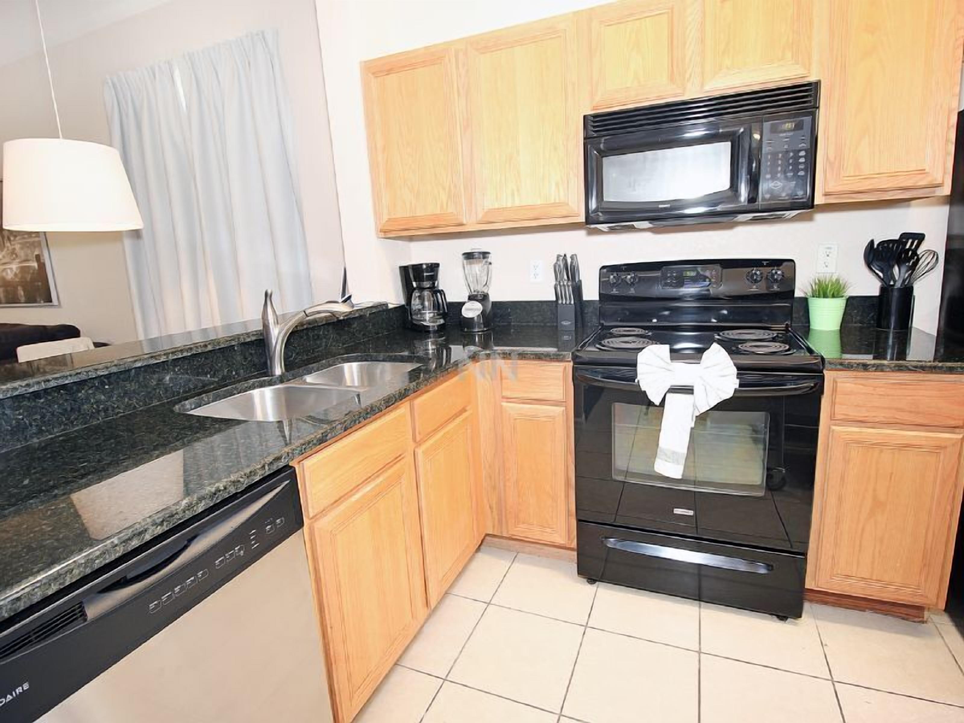 A modern kitchen with granite countertops, wooden cabinets, a black stove, and a microwave.
