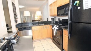 A modern kitchen with a black refrigerator, stainless steel appliances, wooden cabinets, and a tiled floor. - Fv62884 - Regal Oaks - 4 Bed 3.5 Baths Townhome (Kissimmee)