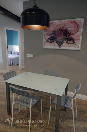 A dining area with a white table and four grey chairs, a black pendant light, and a large abstract painting on the wall. - Free WIFI / AC Buen Suceso Apartment, right in the city center, at Metropol square (Sevilla)