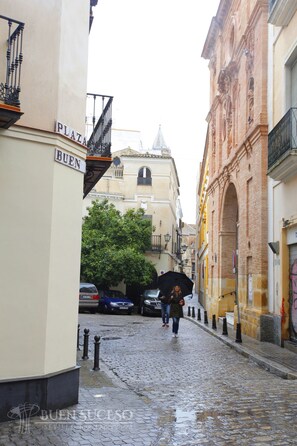 A cobblestone street with buildings on either side, a sign reading "BUEN PLAZA," and a person holding an umbrella. - Free WIFI / AC Buen Suceso Apartment, right in the city center, at Metropol square (Sevilla)