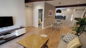 Un salon moderne avec un téléviseur à écran plat, une table basse en bois et un canapé agrémenté de coussins à motifs.