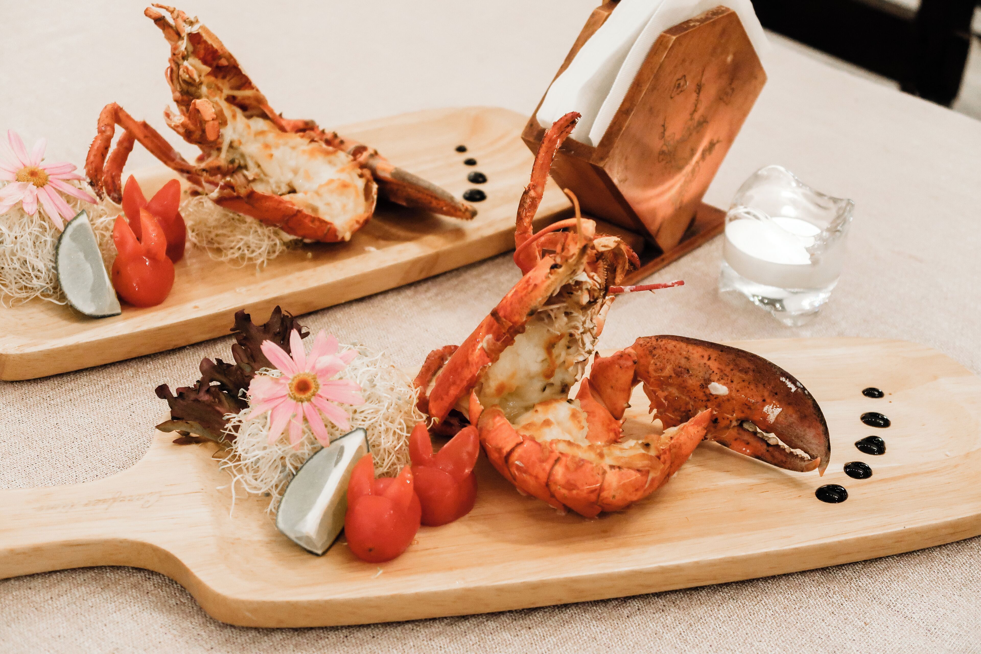 Two lobster halves on wooden serving boards with garnishes and a glass of water.