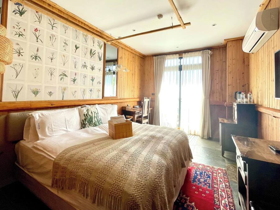 Un dormitorio con una cama grande, paredes de madera, un grabado botánico, un escritorio y un equipo de aire acondicionado.