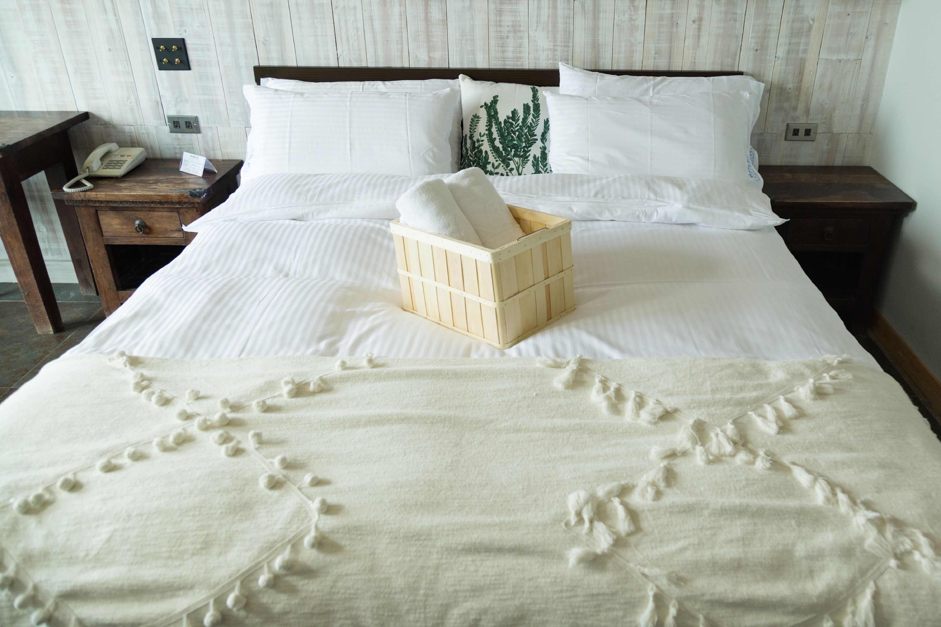A neatly made bed with white linens, a wooden bedside table with a telephone, and a small wooden box on the bed.