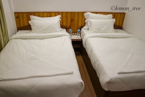 Two single beds with wooden headboards, white bedding, and a nightstand with water bottles and glasses.