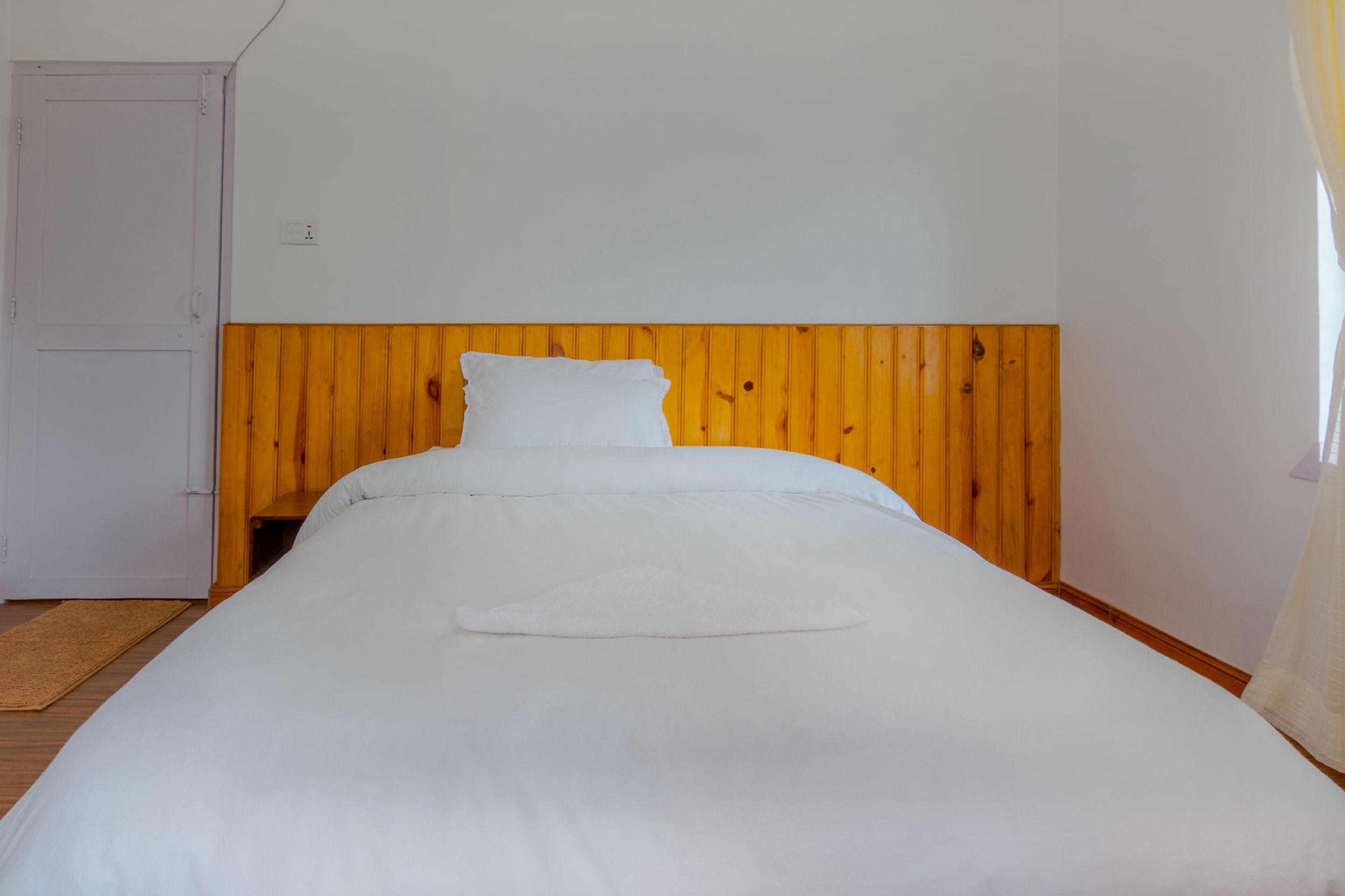 A single bed with a wooden headboard in a room with white walls and a wooden floor.