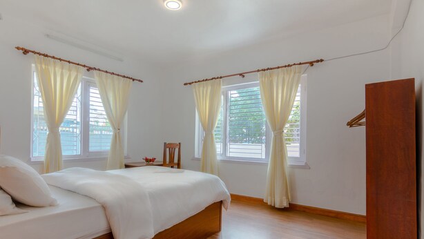 A bedroom with a wooden bed, two windows with curtains, a wooden floor, and a wooden wardrobe. - Lemon Tree Apartment and Homestay (Tohka)